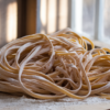 Fresh homemade tagliatelle pasta dusted with flour on wooden surface, wooden spatula beside, natural sunlight through window creating warm, rustic kitchen setting