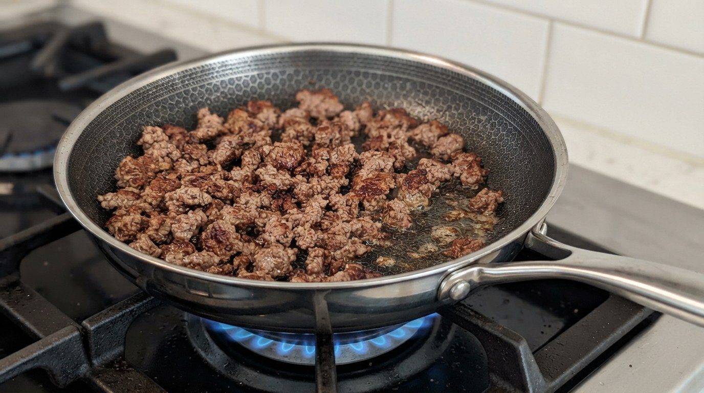 Ground lamb browning in a single layer in a hot skillet, crusty brown edges forming on the crumbles