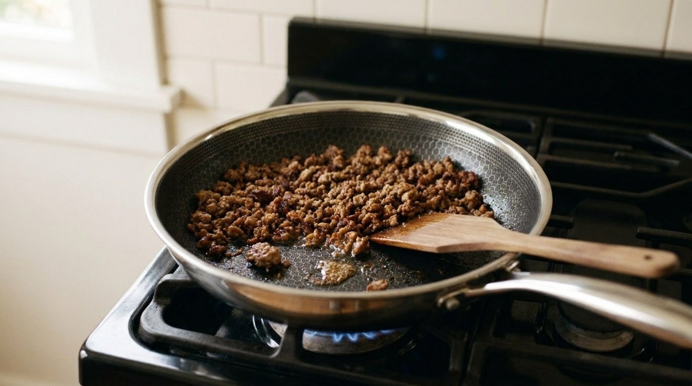 Ground beef for lettuce wraps browning in a thin layer in a hybrid skillet on a gas range, the crumbles deep brown and crisp